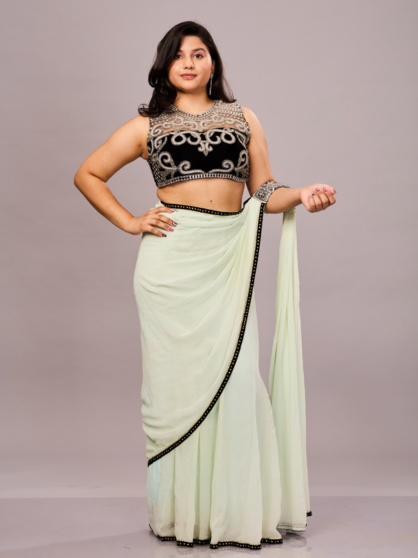 A pastel green saree with a black embellished border, paired with a sleeveless black blouse featuring intricate silver embroidery.