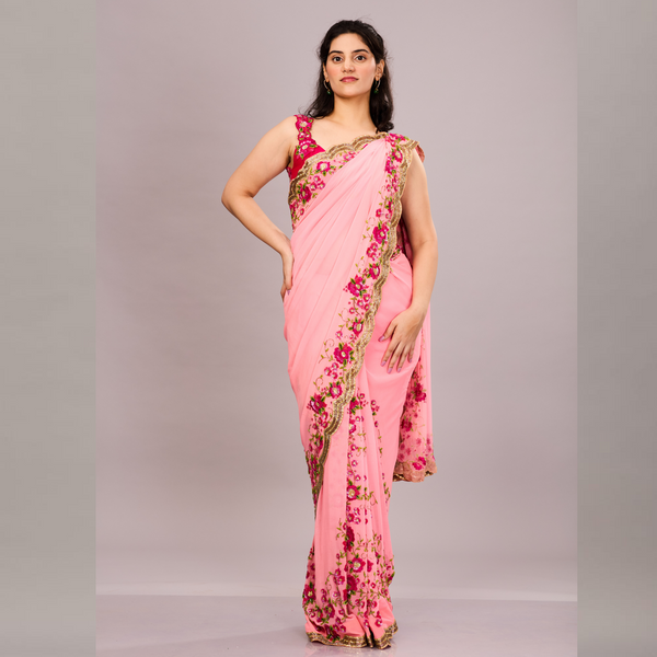 A pink saree with intricate pink and green floral embroidery along the border