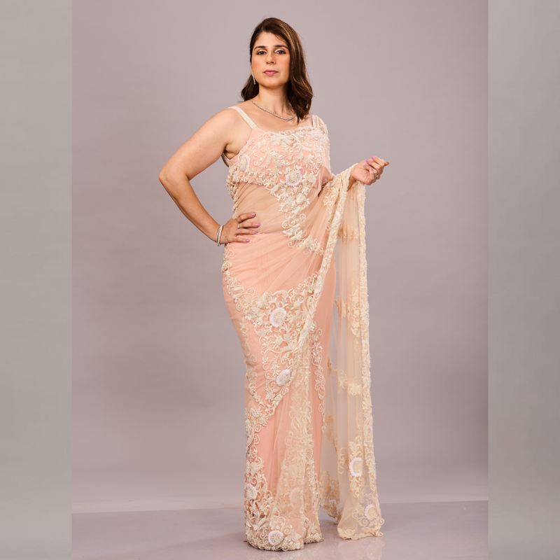 pastel peach net saree with intricate ivory floral embroidery and a matching sleeveless blouse