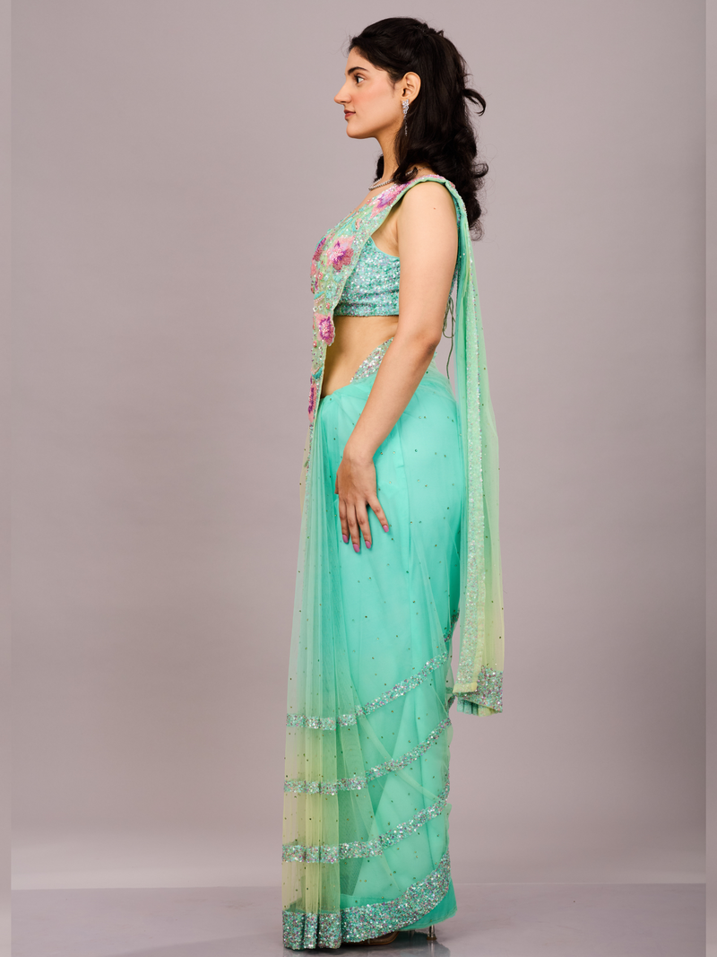 Mint green net saree adorned with sequin borders and paired with a floral embroidered blouse.