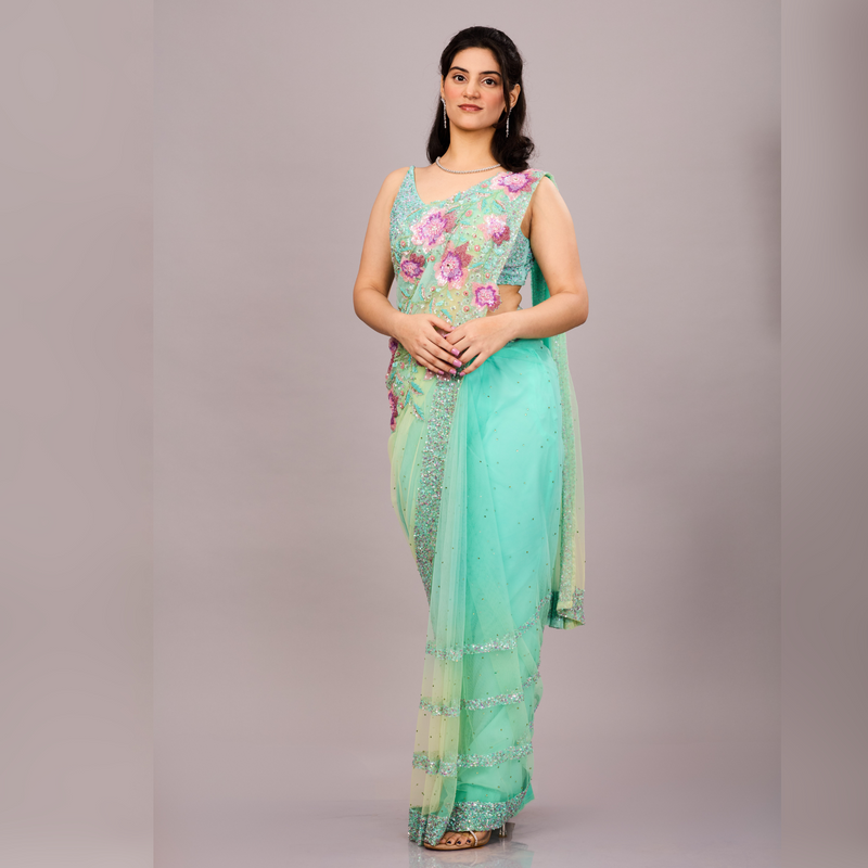 Mint green net saree adorned with sequin borders and paired with a floral embroidered blouse.