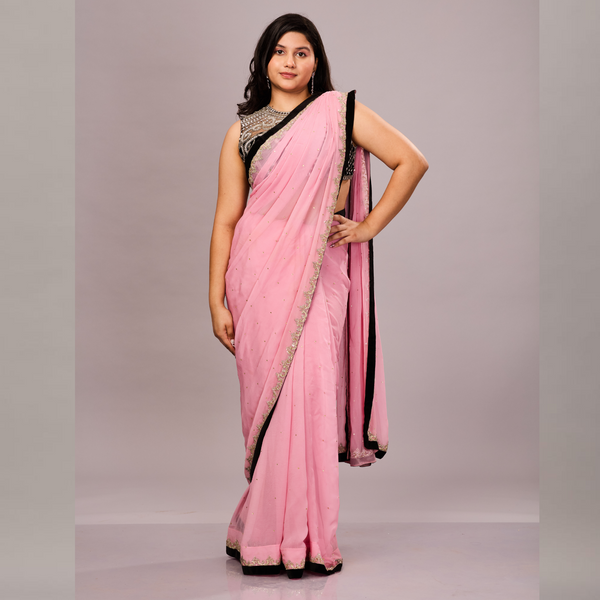 A pastel pink saree with a black and gold embellished border, paired with a sleeveless black blouse featuring intricate silver embroidery.