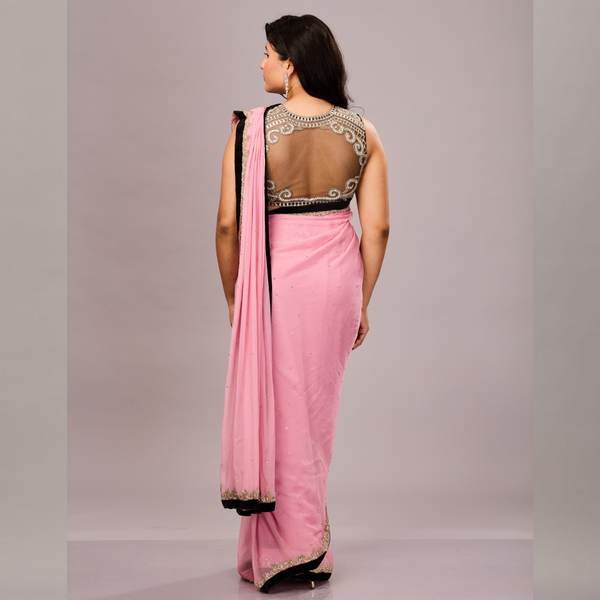 A pastel pink saree with a black and gold embellished border, paired with a sleeveless black blouse featuring intricate silver embroidery.